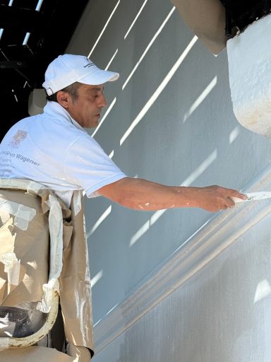 Ein Maler steht auf einer Leiter und streicht eine Wand mit einer Farbrolle.